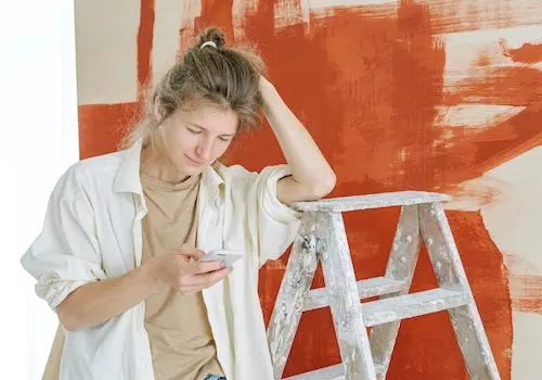 Mulher decorando ambientes em casa com celular na mão