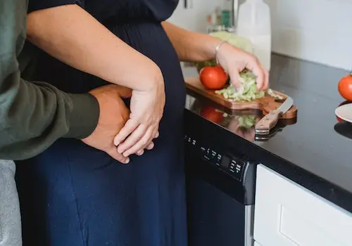 mulher grávida e seu esposo se abraçam na cozinha enquanto preparam uma alimentação saudável 